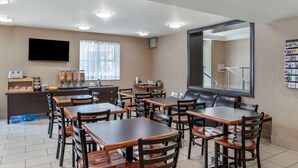 A hotel dining area with multiple tables and chairs, a television mounted on the wall, and a large mirror reflecting the room. - EconoLodge Downtown Toronto (Toronto)