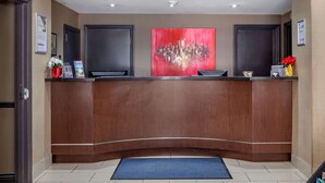 A reception desk with a curved design, a red abstract painting above it, and a blue mat at the entrance. - EconoLodge Downtown Toronto (Toronto)