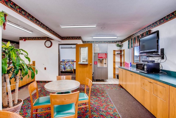 A small, cozy room with a round table and chairs, a refrigerator, a microwave, a television, and a vending machine.