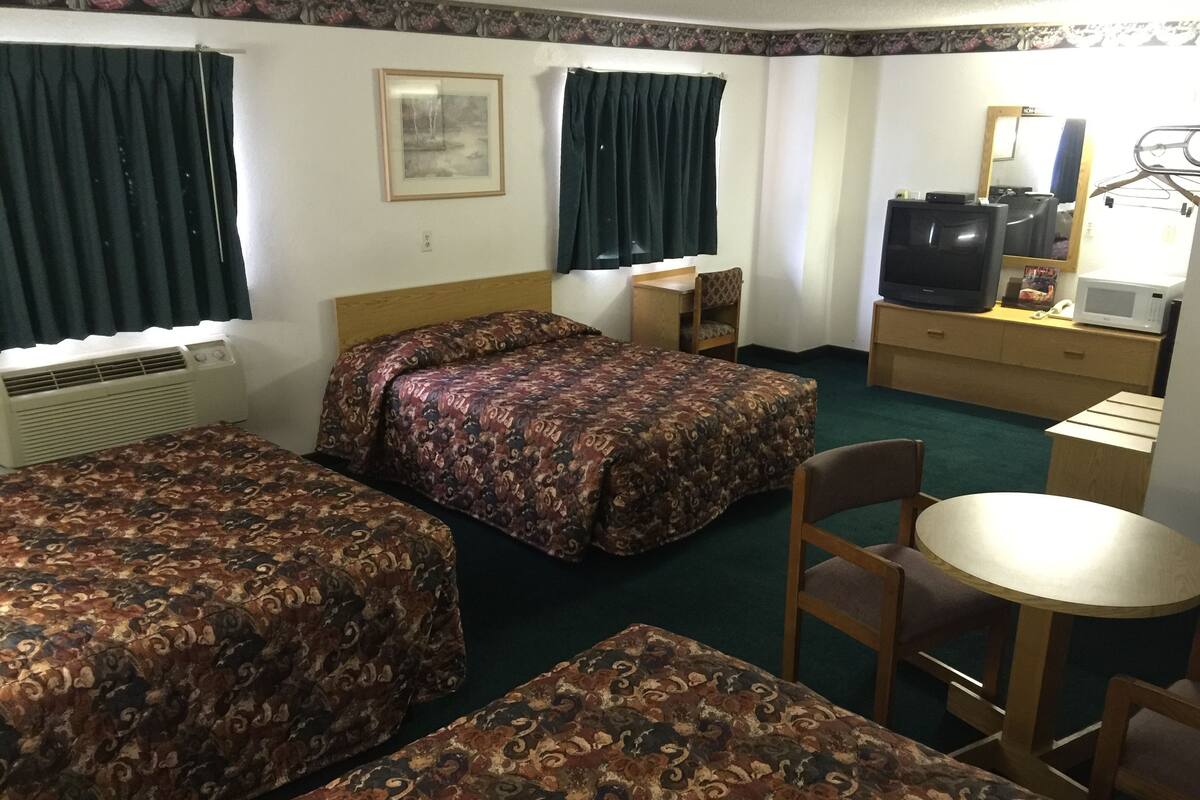 A hotel room with two beds, a desk, a chair, a television, and a mirror.