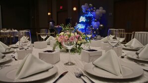 Una mesa de comedor formal con manteles blancos, cristalería y un centro de mesa con flores.