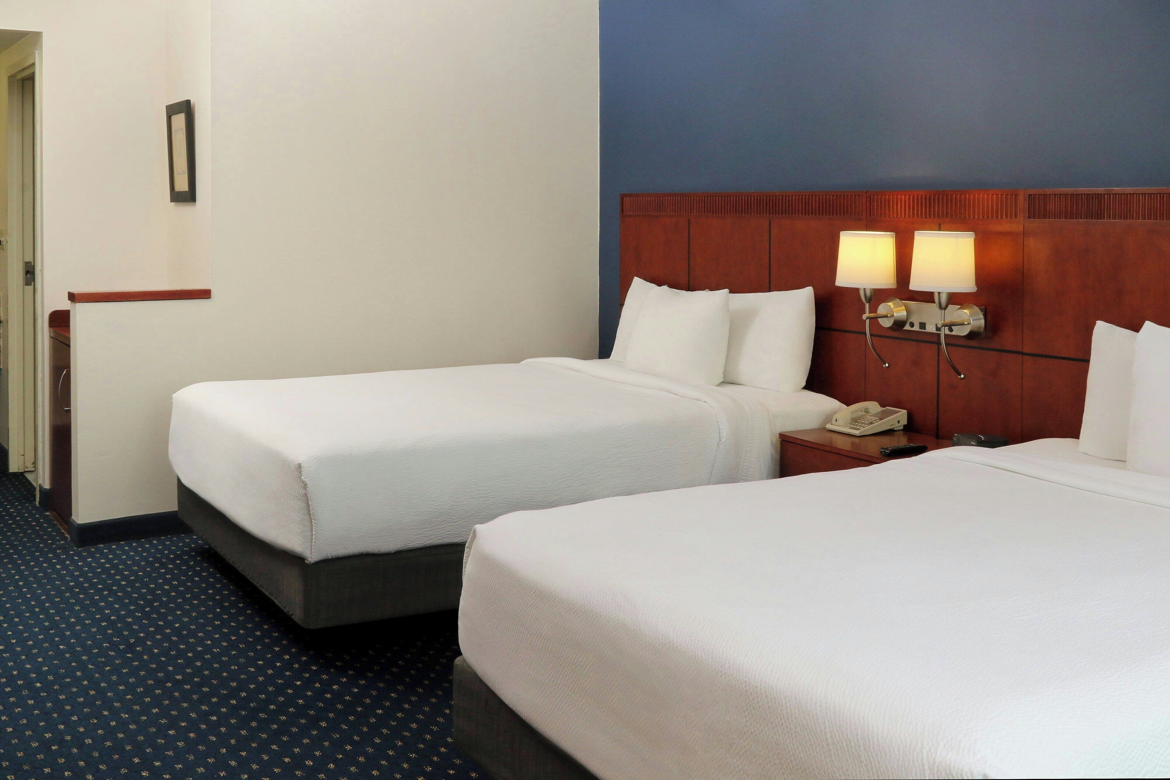 A hotel room with two beds, a wooden headboard, bedside lamps, a telephone, and a small table.