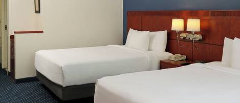 A hotel room with two beds, a wooden headboard, bedside lamps, a telephone, and a small table.