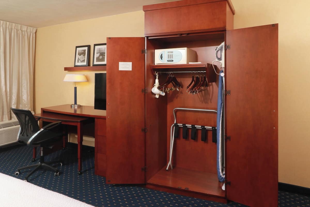 A hotel room with a wooden wardrobe, a desk with a lamp, and a chair.