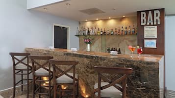 A bar area with a marble countertop, three wooden bar stools, and a variety of liquor bottles.