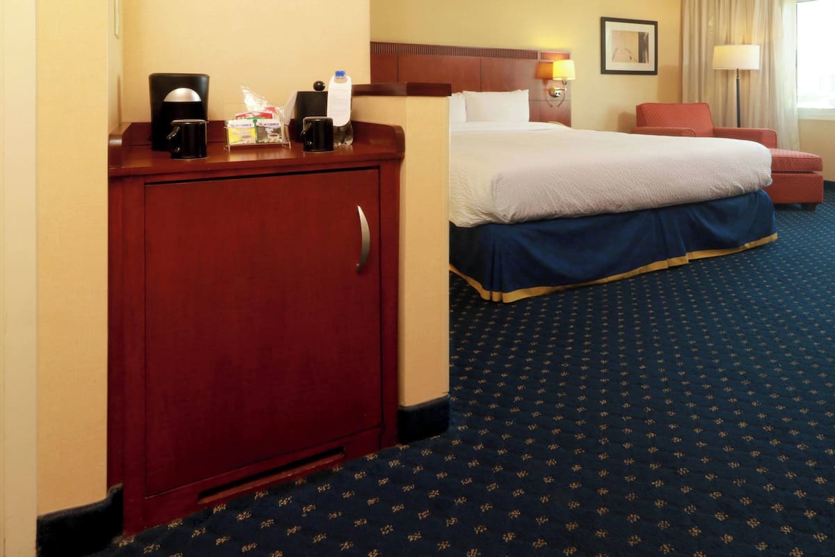A hotel room with a bed, a desk with a coffee maker, a red cabinet, and a patterned carpet.