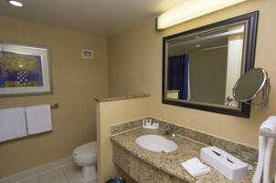 Un baño con lavamanos, espejo e inodoro. Hay toallas y un cuadro en la pared.