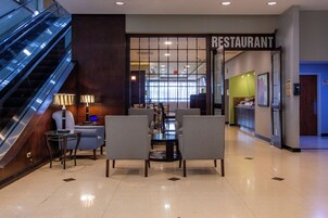 Vestíbulo de hotel con escalera, zona de estar y entrada a un restaurante.