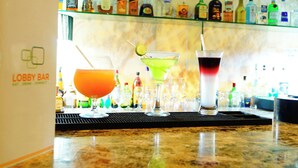 Zona de bar con tres cócteles sobre la barra, un estante de vidrio con varias botellas de licor al fondo, y un letrero que dice 