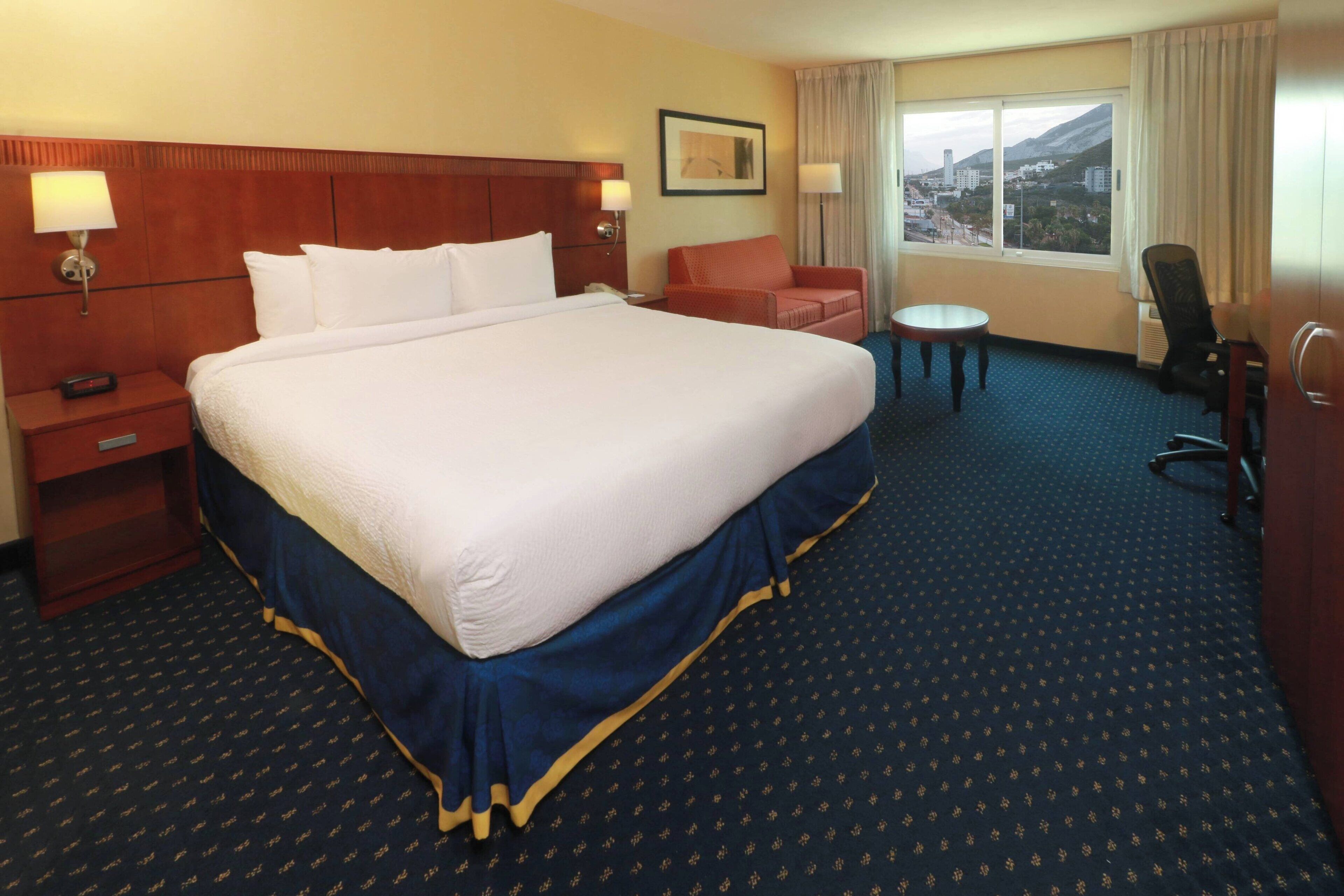 Habitación de hotel con una cama grande, un escritorio, una silla y vista a la ciudad.