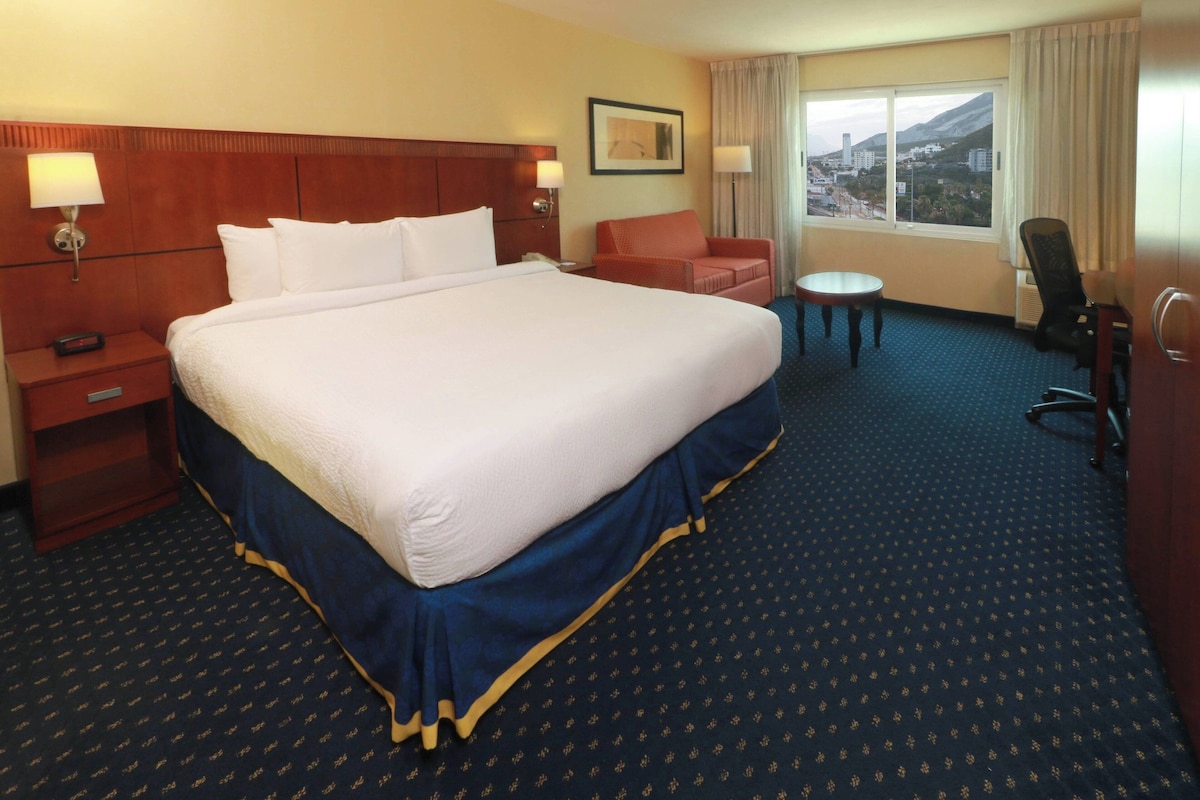 Habitación de hotel con una cama grande, un escritorio, una silla y vista a la ciudad.