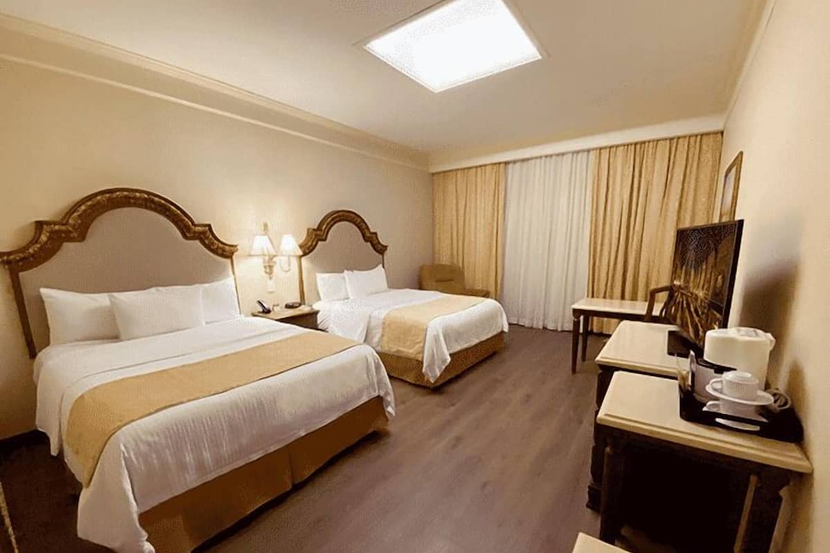 Habitación de hotel con dos camas, un escritorio, una silla, una lámpara y un cuadro en la pared.