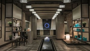 Een modern interieur met een centraal waterkunstwerk, planken met producten en een ronde lamp aan de muur.