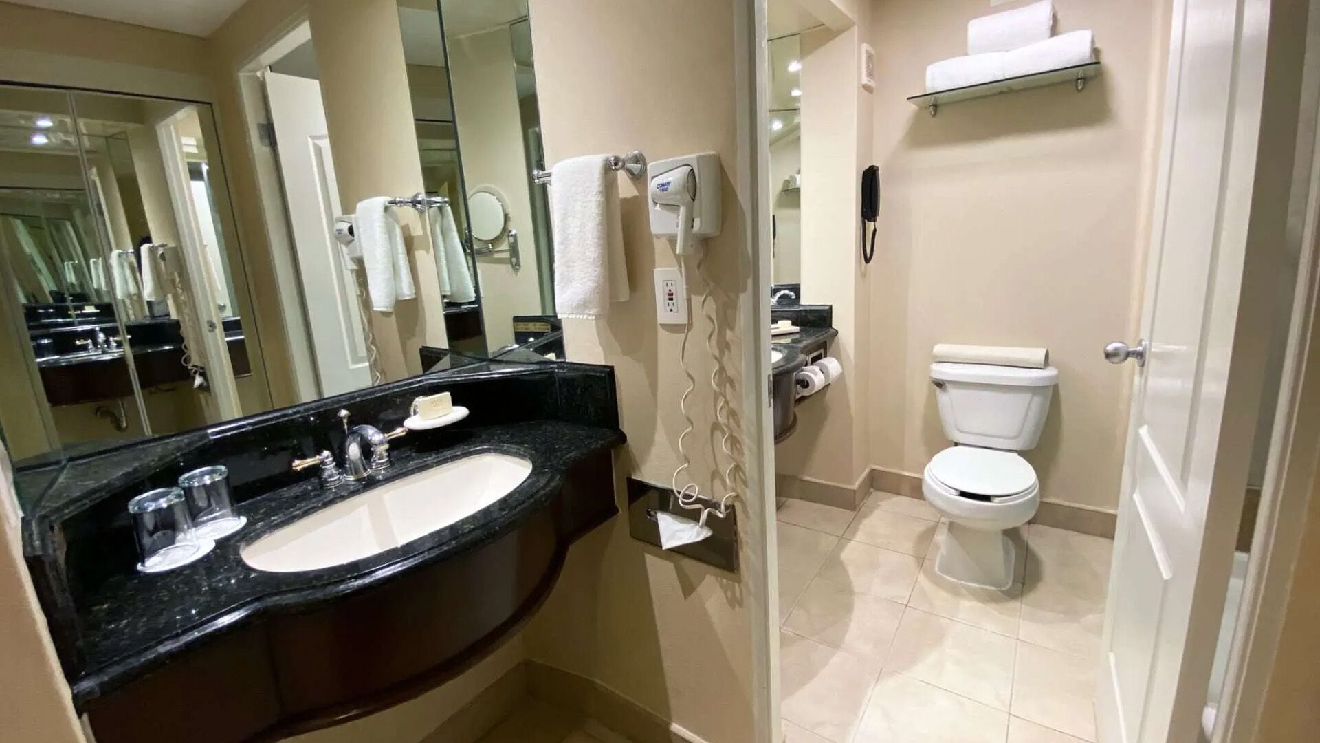 A bathroom with a black countertop sink, a toilet, a mirror, and a towel rack.