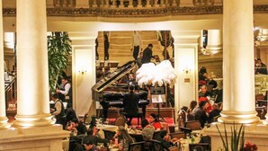 Een statige eetzaal met hoge plafonds, versierde zuilen en een piano in het midden.