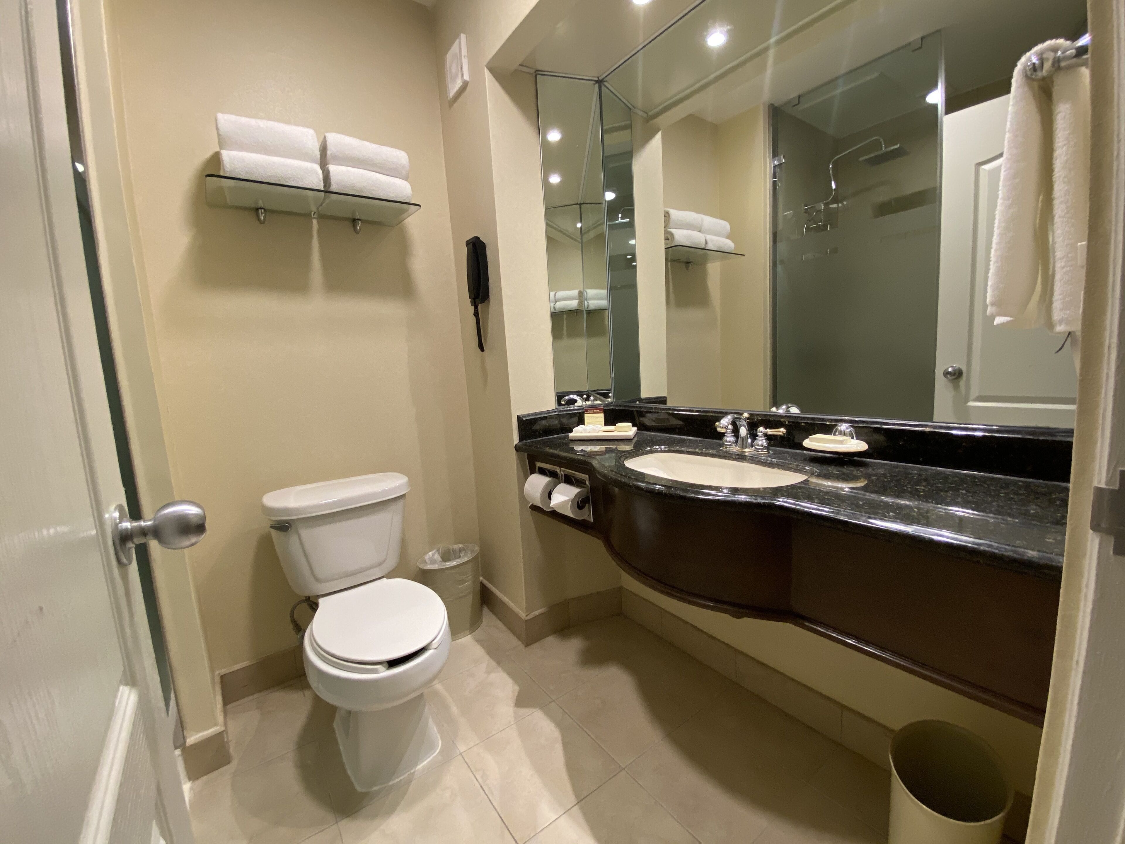 A bathroom with a toilet, sink, and mirror. There are towels on a shelf above the toilet.