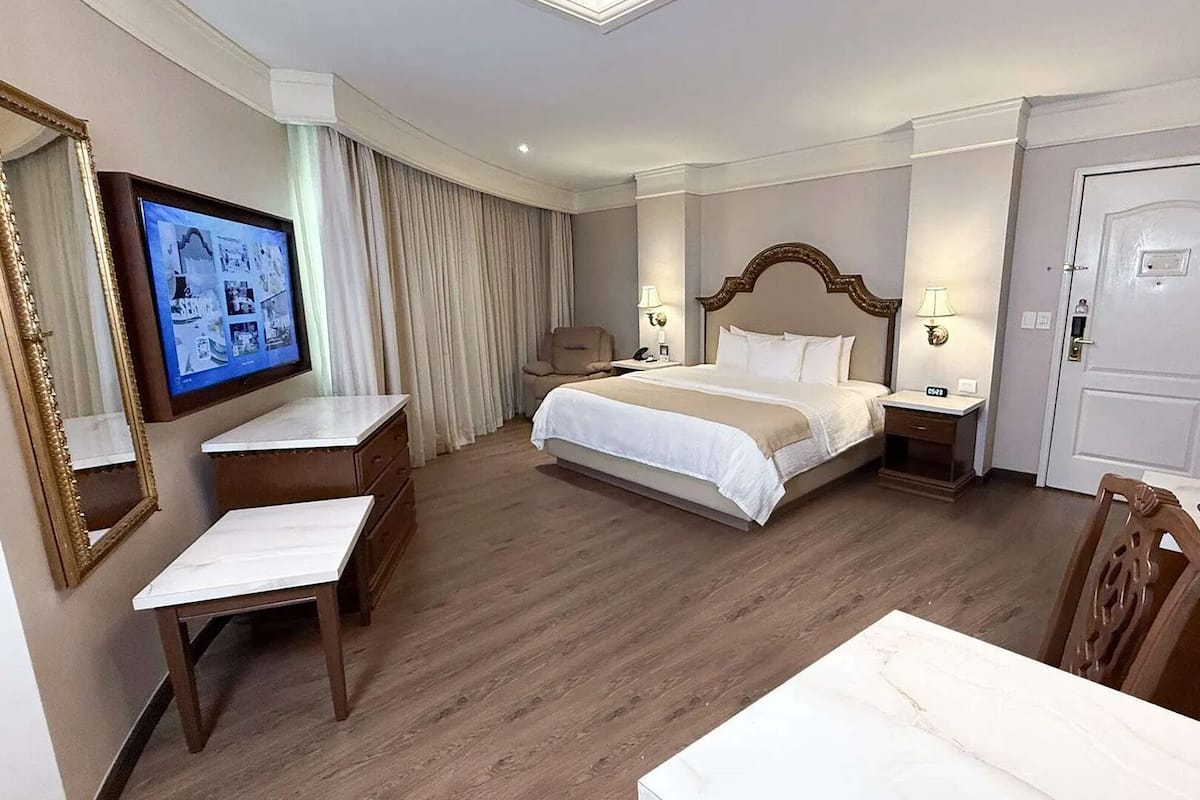 Una habitación de hotel con cama, escritorio, silla, televisor y puerta.