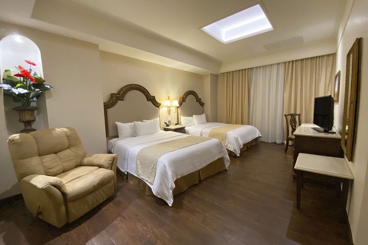 Habitación de hotel con dos camas, un escritorio, una silla, un televisor y un tragaluz.
