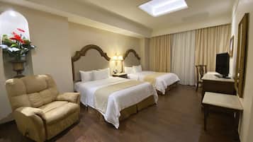 A hotel room with two beds, a desk, a chair, a TV, and a skylight.