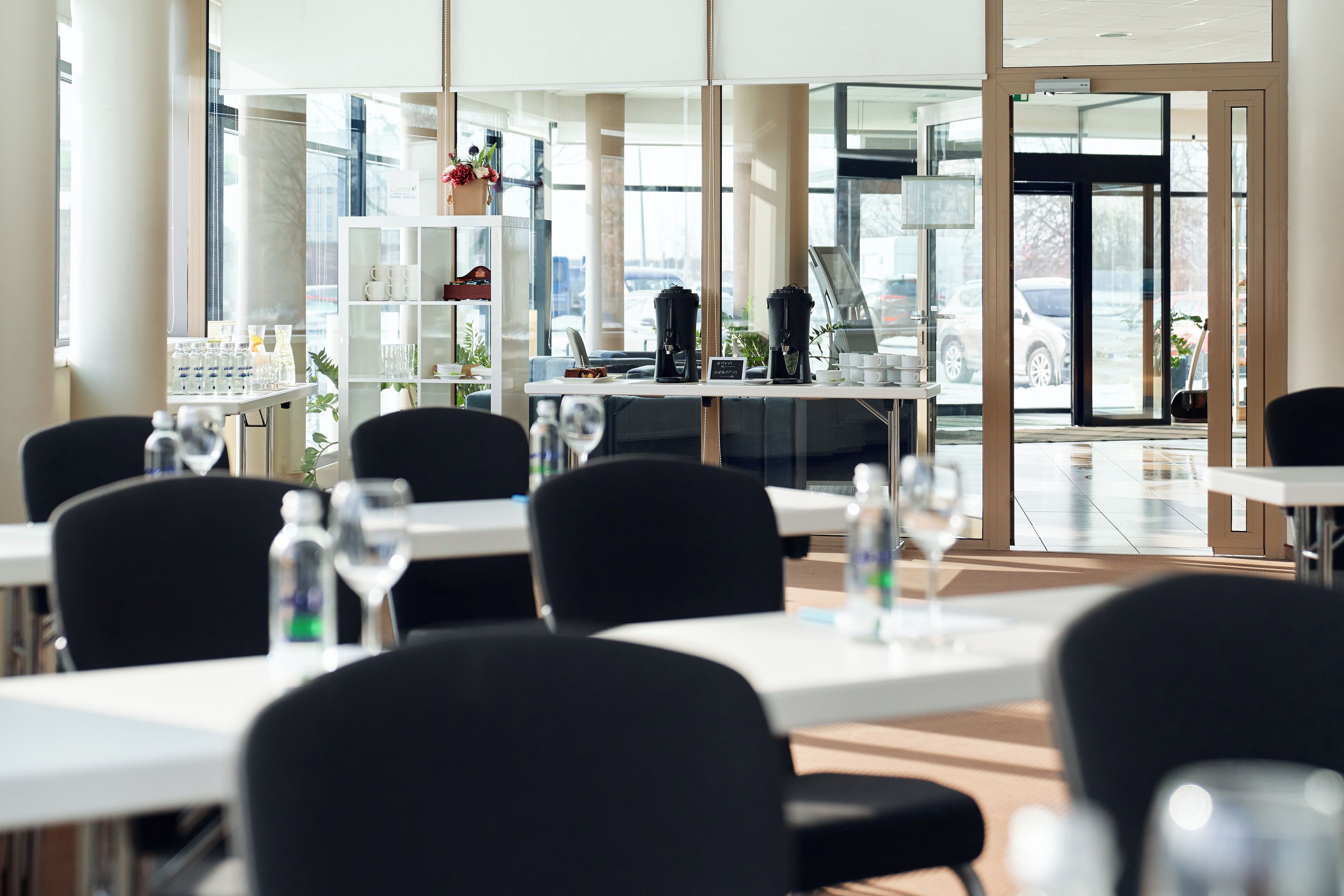 A modern hotel lobby with a seating area, a coffee station, and a view of the parking lot.