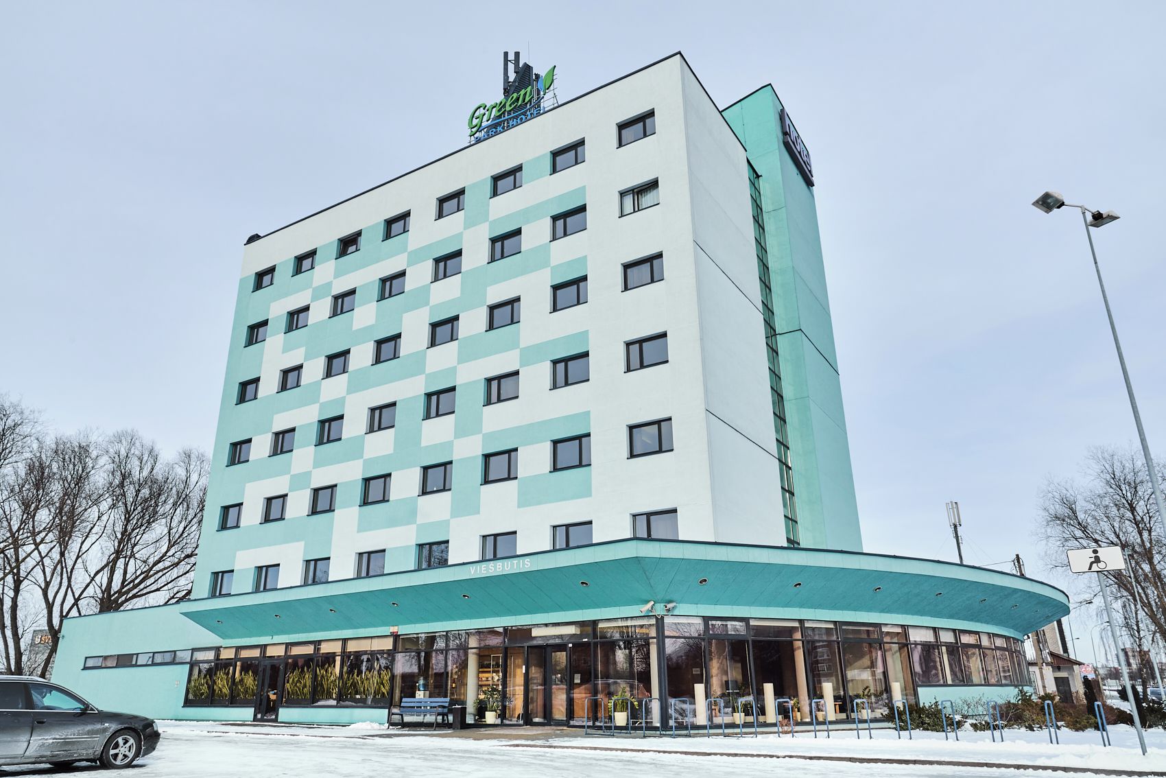 Un hotel de varios pisos con fachada plana, amplias ventanas y un área de entrada curva con asientos al aire libre.