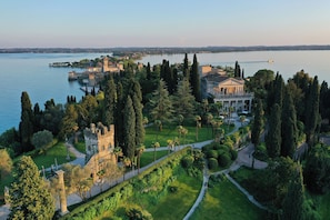 A historic estate with a large lawn, a castle-like structure, and a body of water in the background. - Villa Cortine Palace Relais Chateaux (Sirmione)