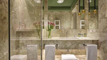 Un bagno con pareti in marmo, box doccia in vetro, lavabo con specchio sopra e asciugamani sul pavimento.