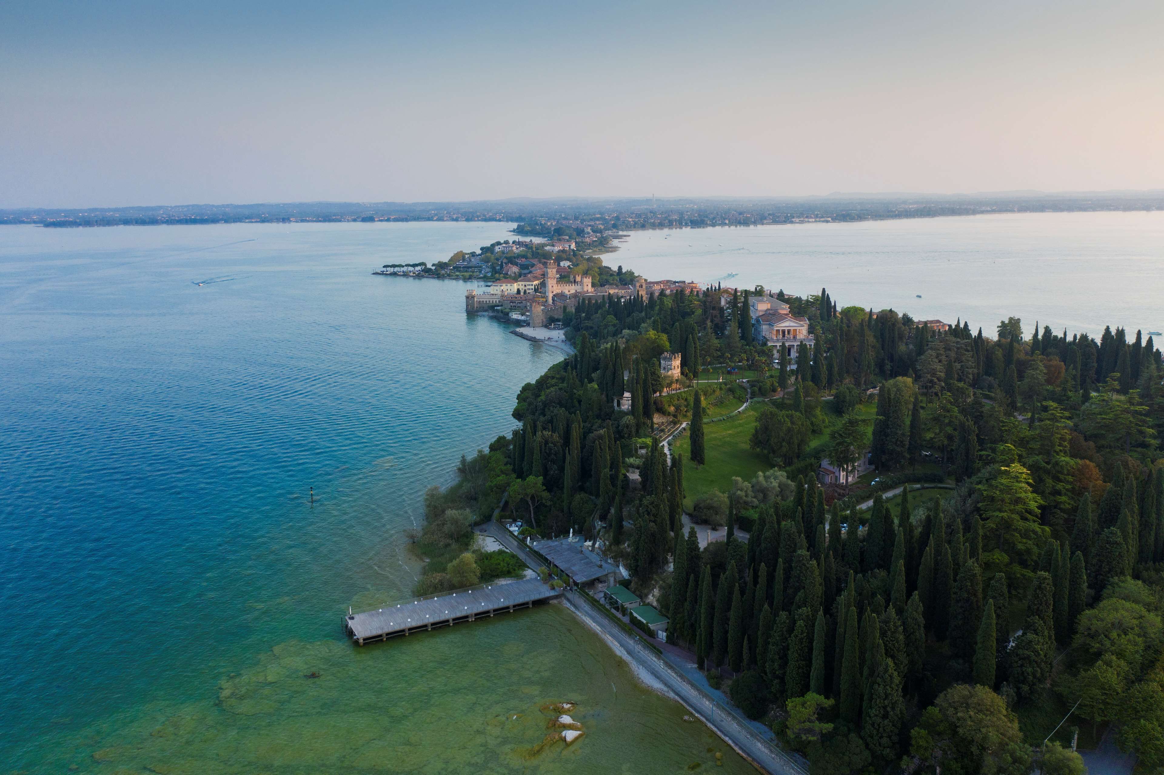 An aerial view of a coastal property with a large body of water, a castle-like structure, and dense greenery.
