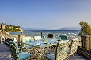 An outdoor dining area with a table and chairs, overlooking a body of water and mountains. - Villa Cortine Palace Relais Chateaux (Sirmione)