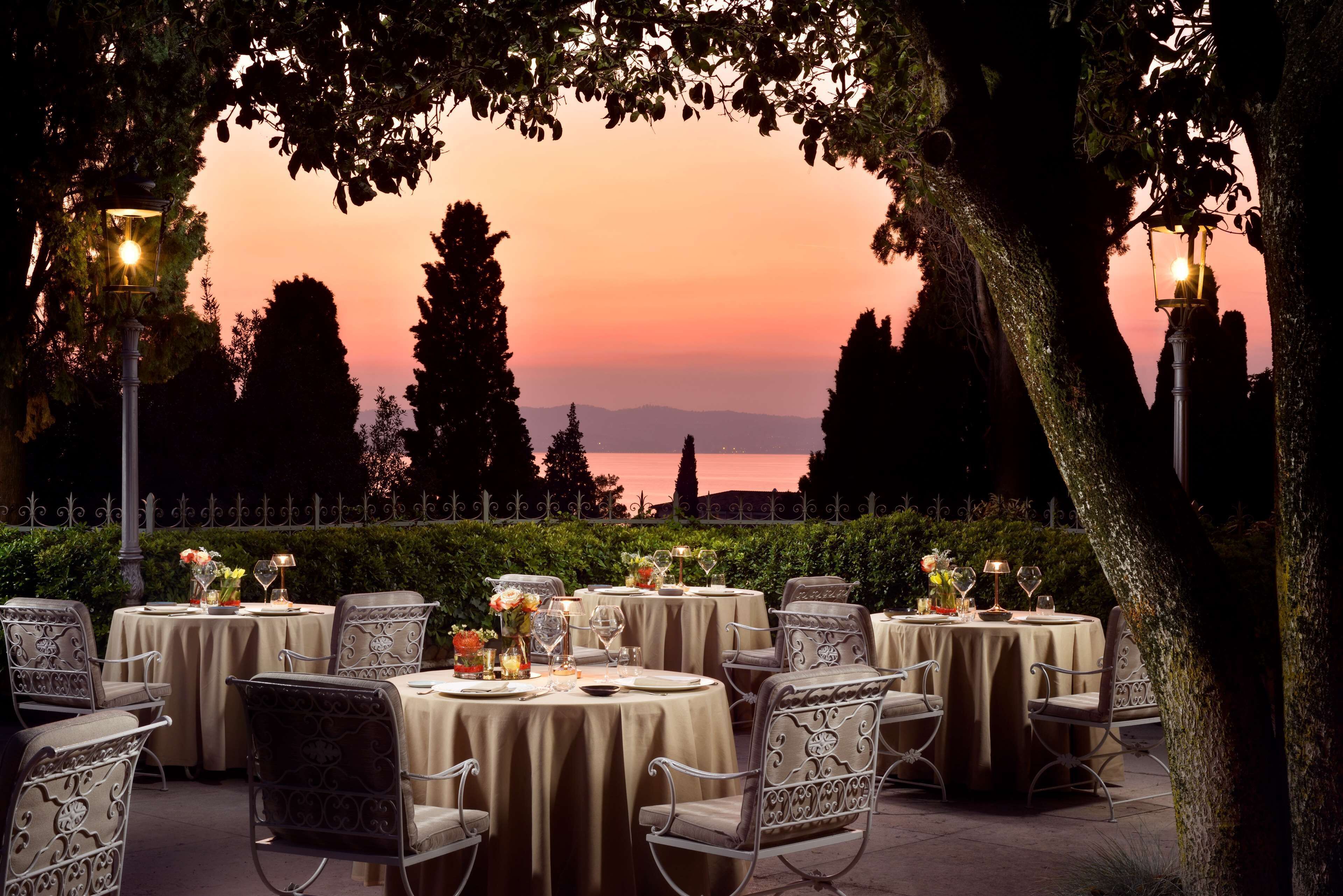 An outdoor dining area with round tables and chairs, set against a sunset backdrop.