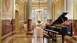 Un vaste hall d’entrée agrémenté d’un magnifique piano à queue noir, de colonnes richement décorées et d’un lustre.