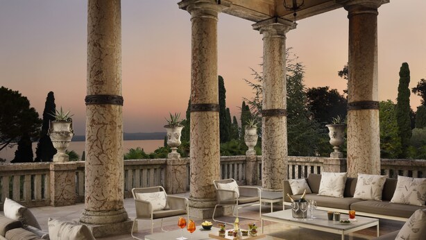 Un espace extérieur luxueux, aménagé avec des colonnes de marbre, des canapés et une table basse sur laquelle sont disposées des boissons et des en-cas.