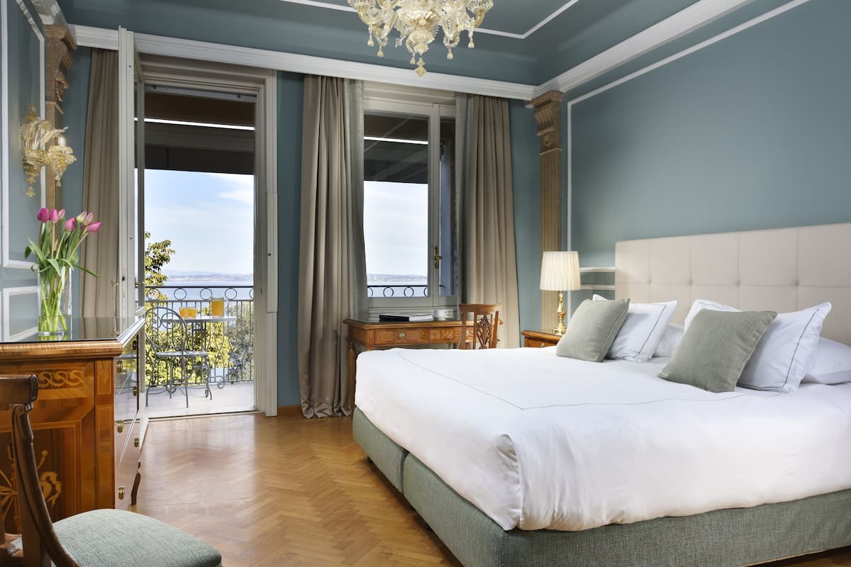 Un dormitorio amplio con una cama grande, un escritorio de madera, una silla y vistas al exterior desde un balcón.