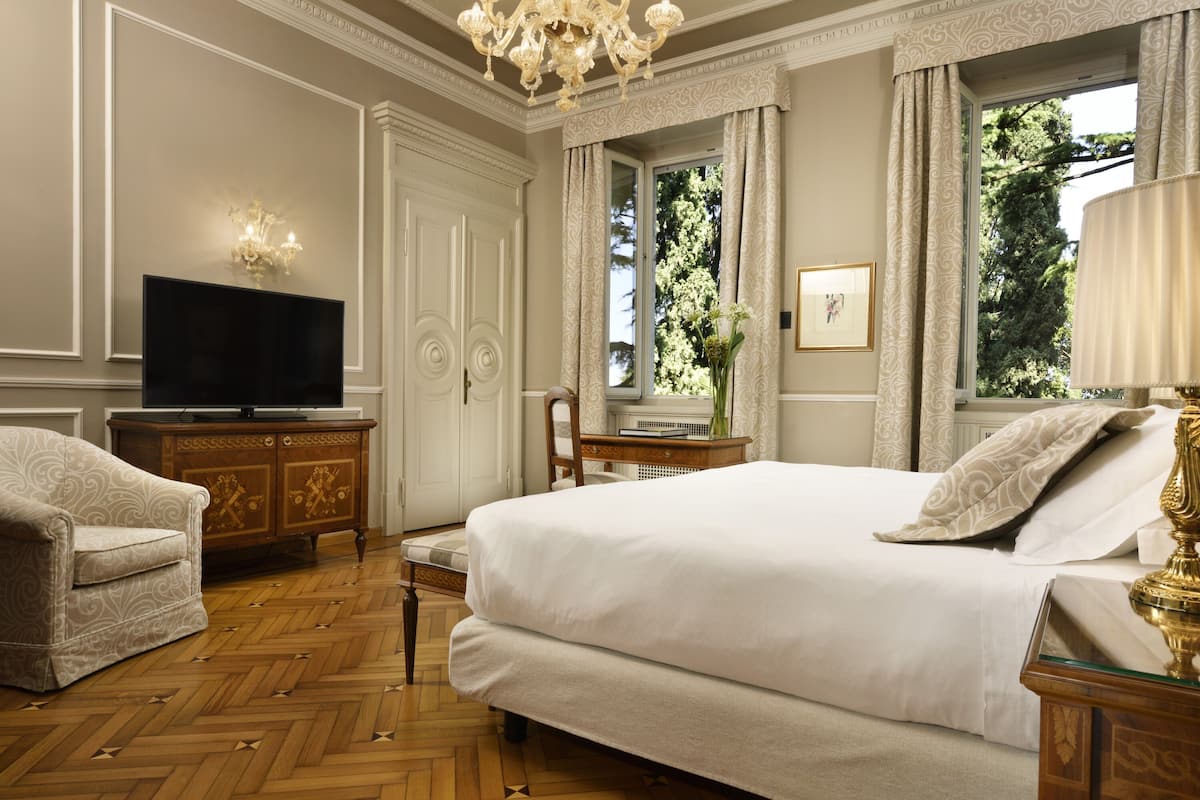 Habitación de hotel con una cama grande, televisión, aparador de madera y una silla.
