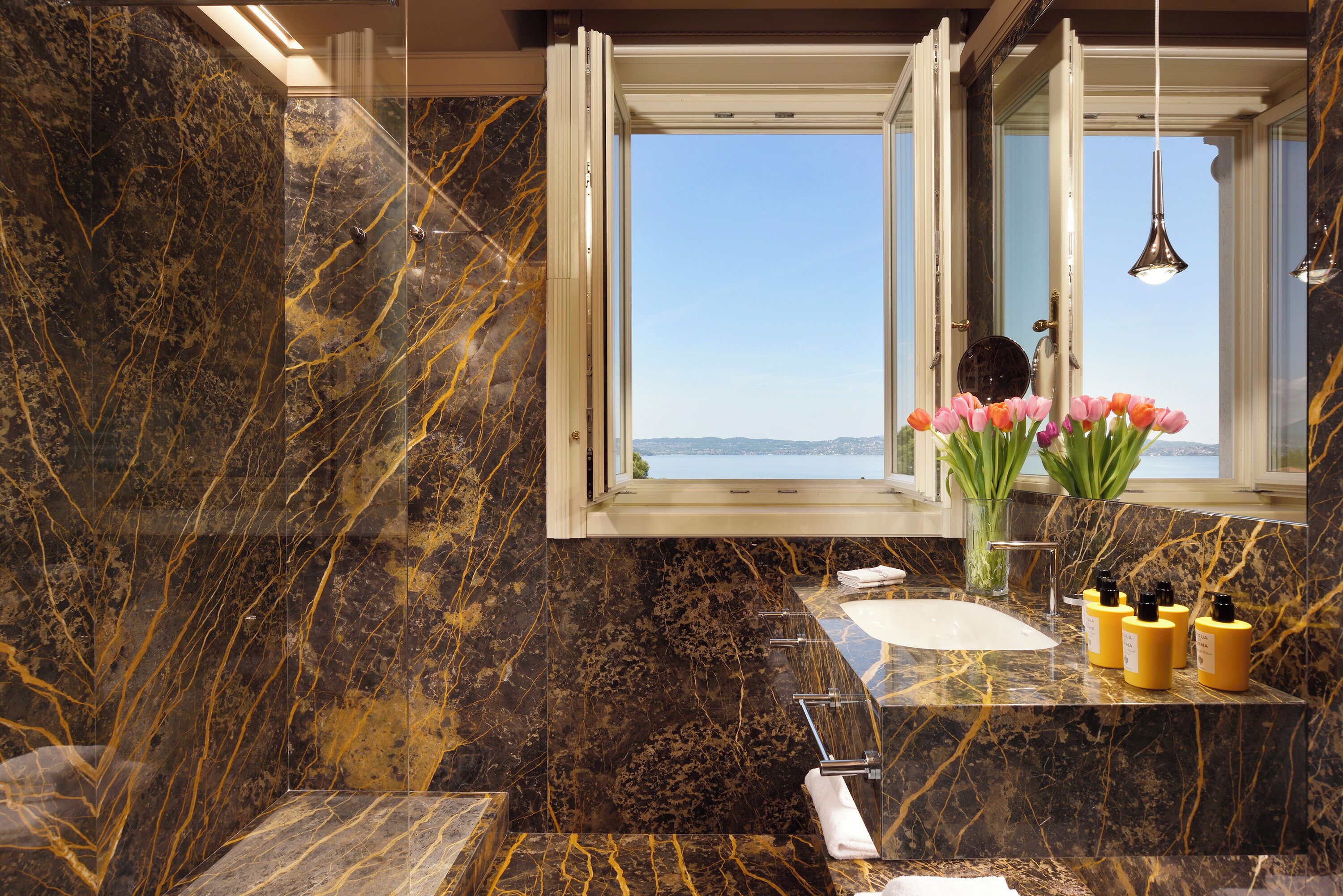 Une salle de bain avec un lavabo en marbre, une fenêtre donnant sur un beau paysage et un vase rempli de fleurs.