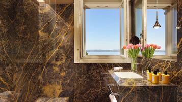 Une salle de bain avec un lavabo en marbre, une fenêtre donnant sur un beau paysage et un vase rempli de fleurs.