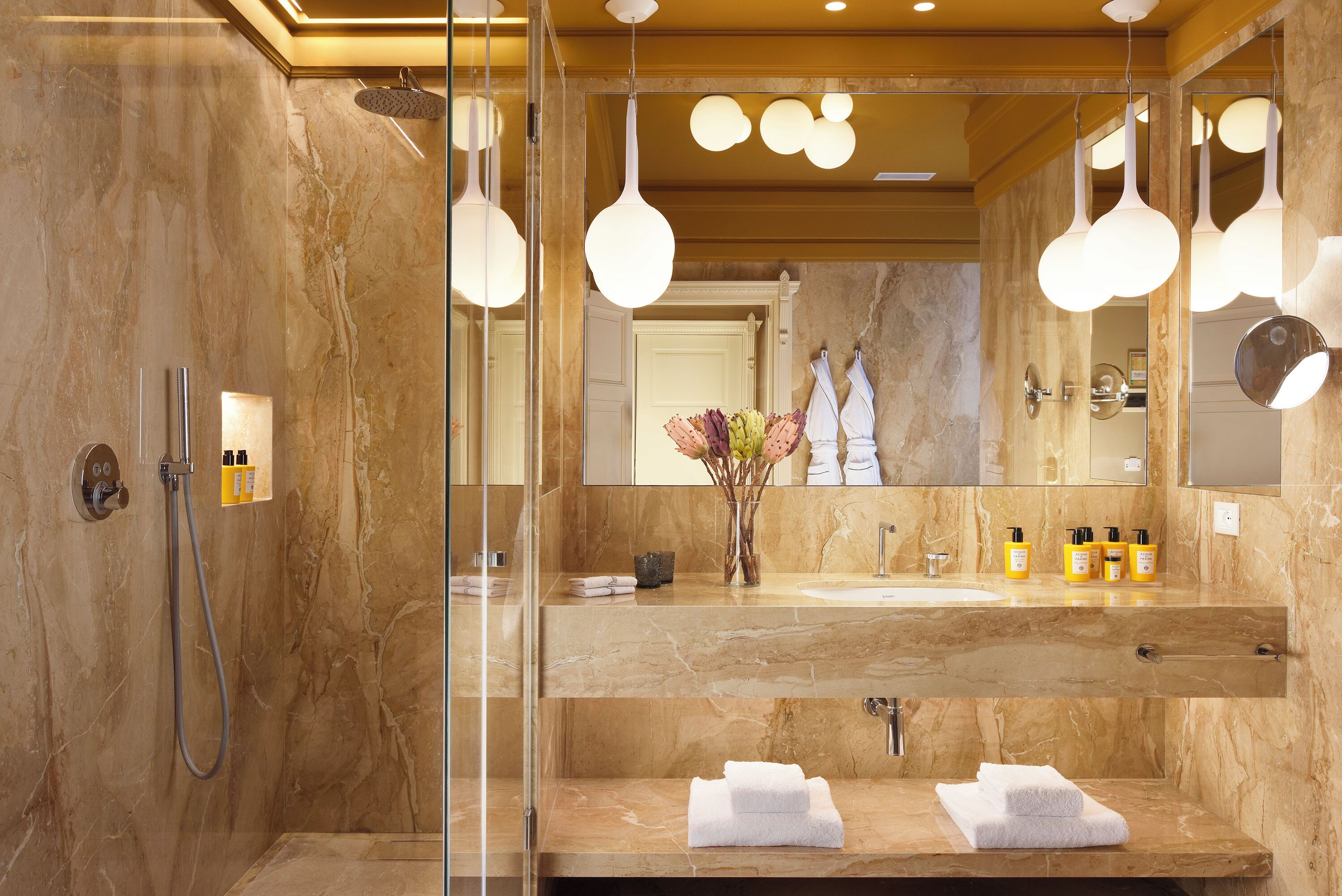 Un baño moderno con ducha envuelta en vidrio, tocador de mármol y un espejo grande.