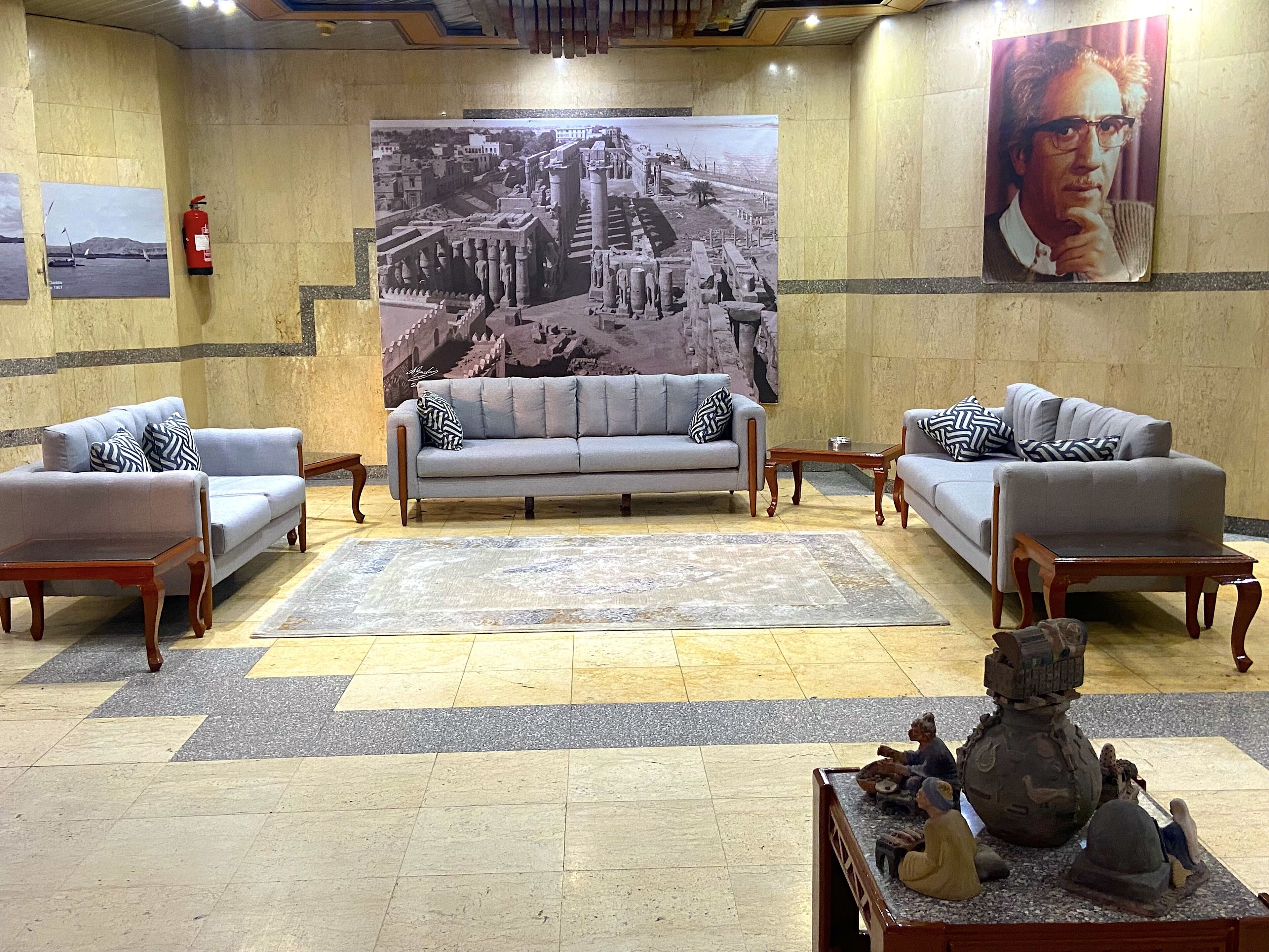 Un vestíbulo con dos sofás grises, una mesa de centro, un tapete estampado y un gran mural histórico en la pared.