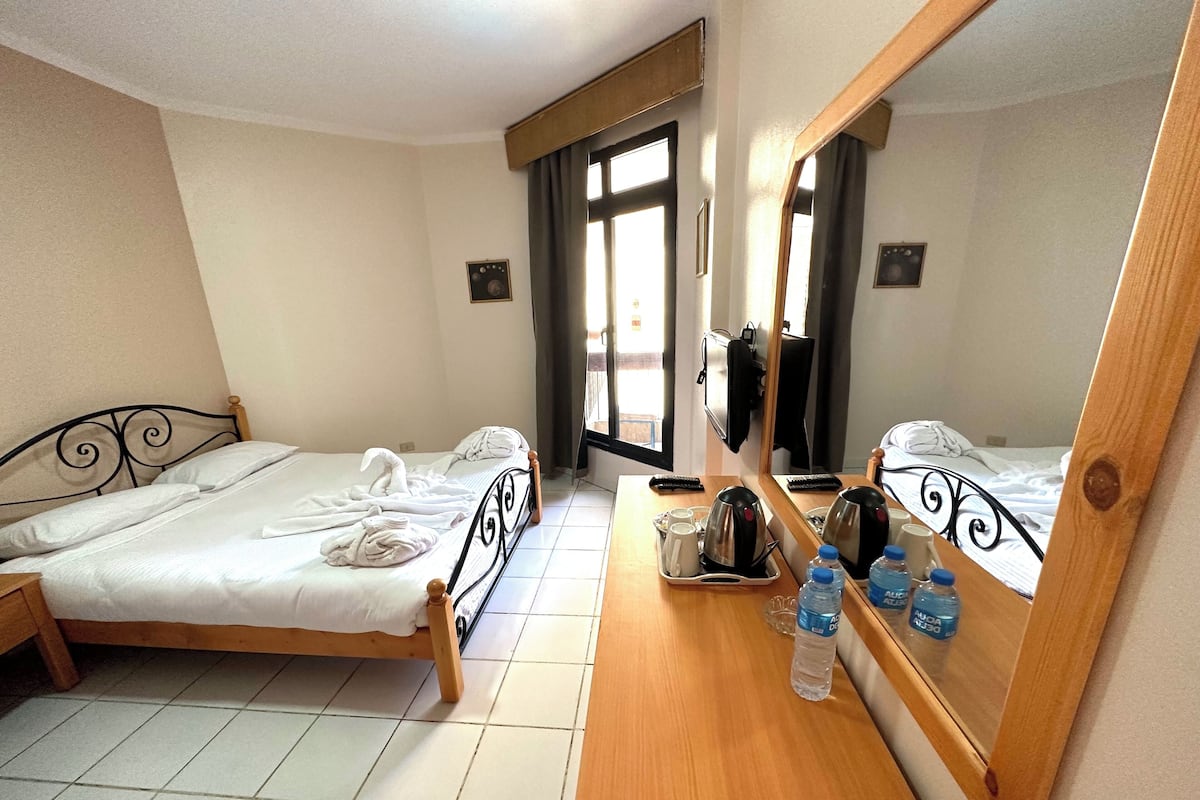 A hotel room with two beds, a wooden dresser, a mirror, and a window with curtains.