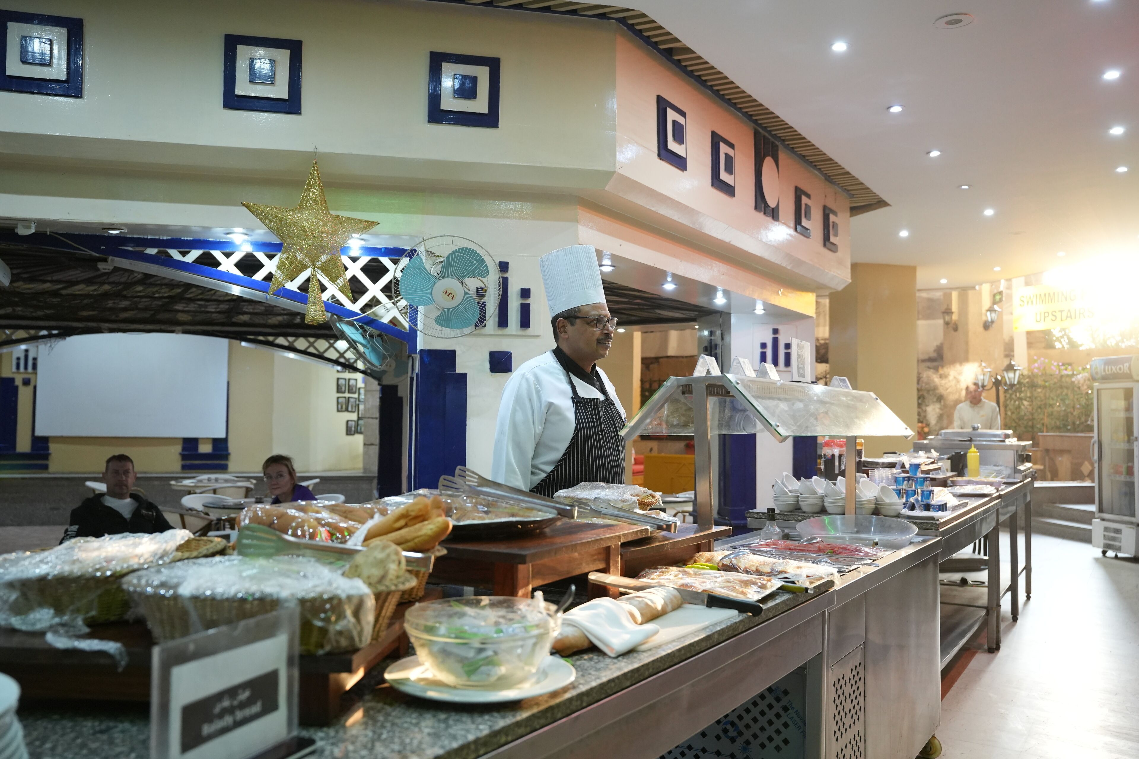 A buffet area with various food items and a chef in uniform.