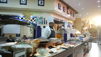 A buffet area with various food items and a chef in uniform.
