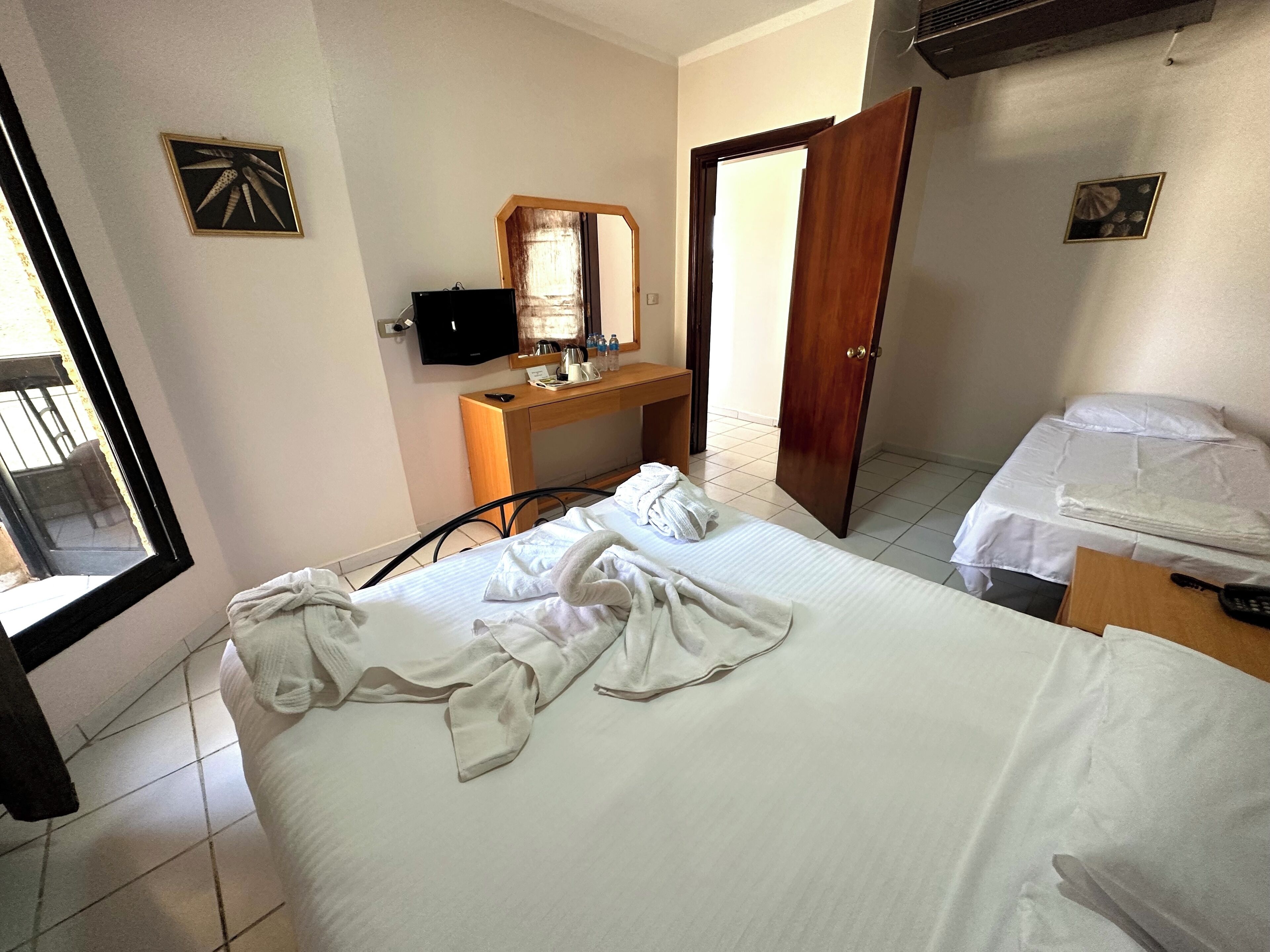 A hotel room with a bed, a desk with a computer, a TV, and a door.