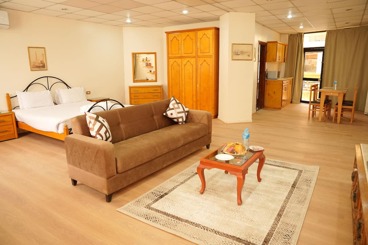 A hotel room with a bed, sofa, dining table, kitchen area, and a wardrobe.