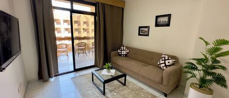 A living room with a sofa, a coffee table, a TV, a sliding glass door leading to a balcony, and a potted plant.