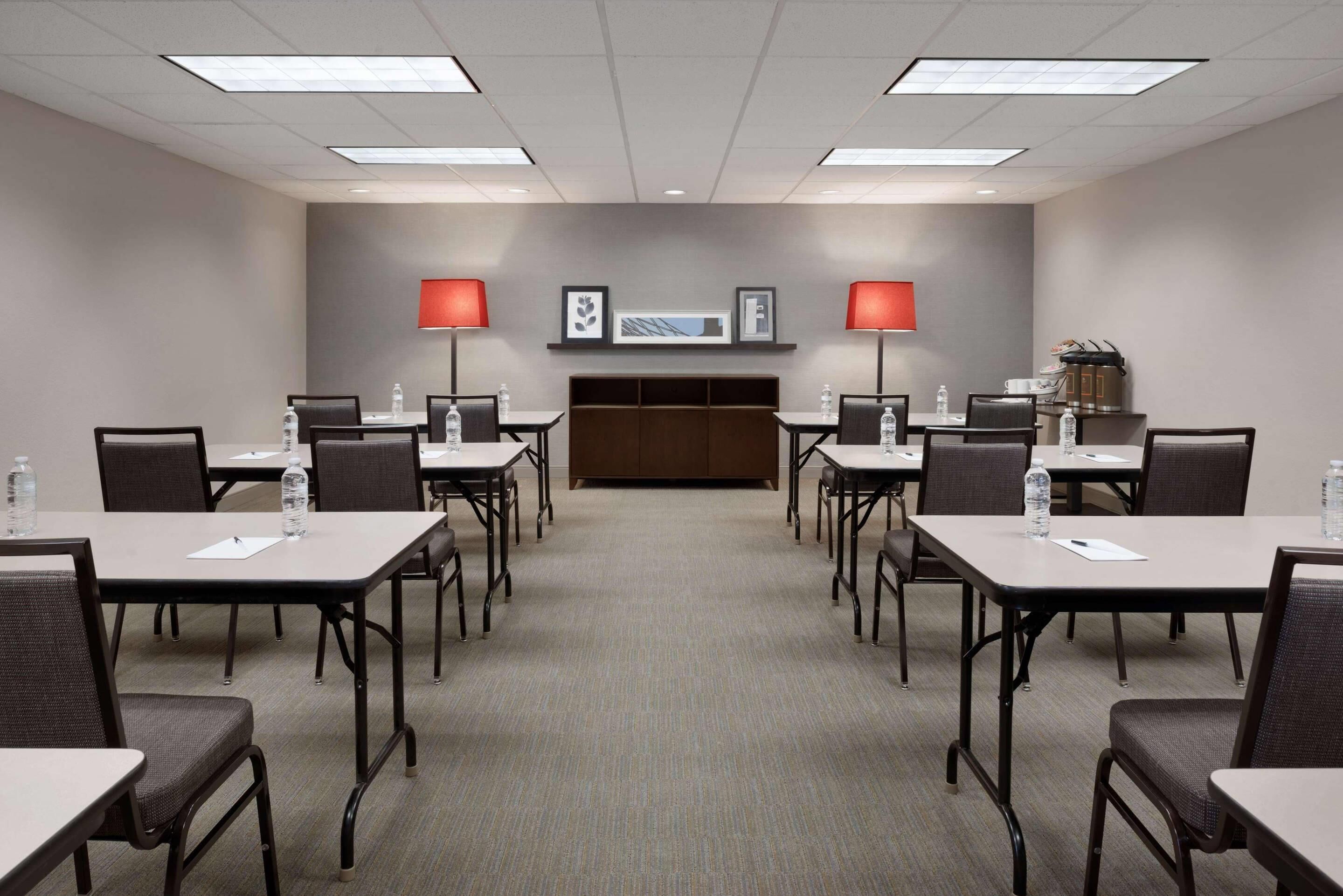 Une salle de conférence dotée de plusieurs tables et chaises, équipée de bouteilles d’eau et de documents, et présentant une décoration aux couleurs neutres et un design moderne.