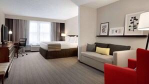 A hotel room with a bed, a desk, a chair, a sofa, and a TV. - Country Inn & Suites by Radisson, Houghton, MI (Houghton)