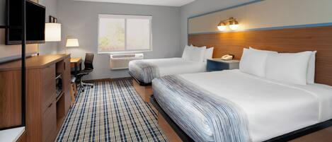 A hotel room with two beds, a desk, a chair, a TV, a lamp, a phone, and a window.