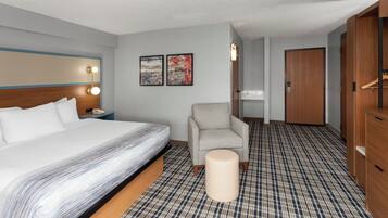 A hotel room with a bed, a chair, a small table, a wardrobe, and two wall-mounted artworks.