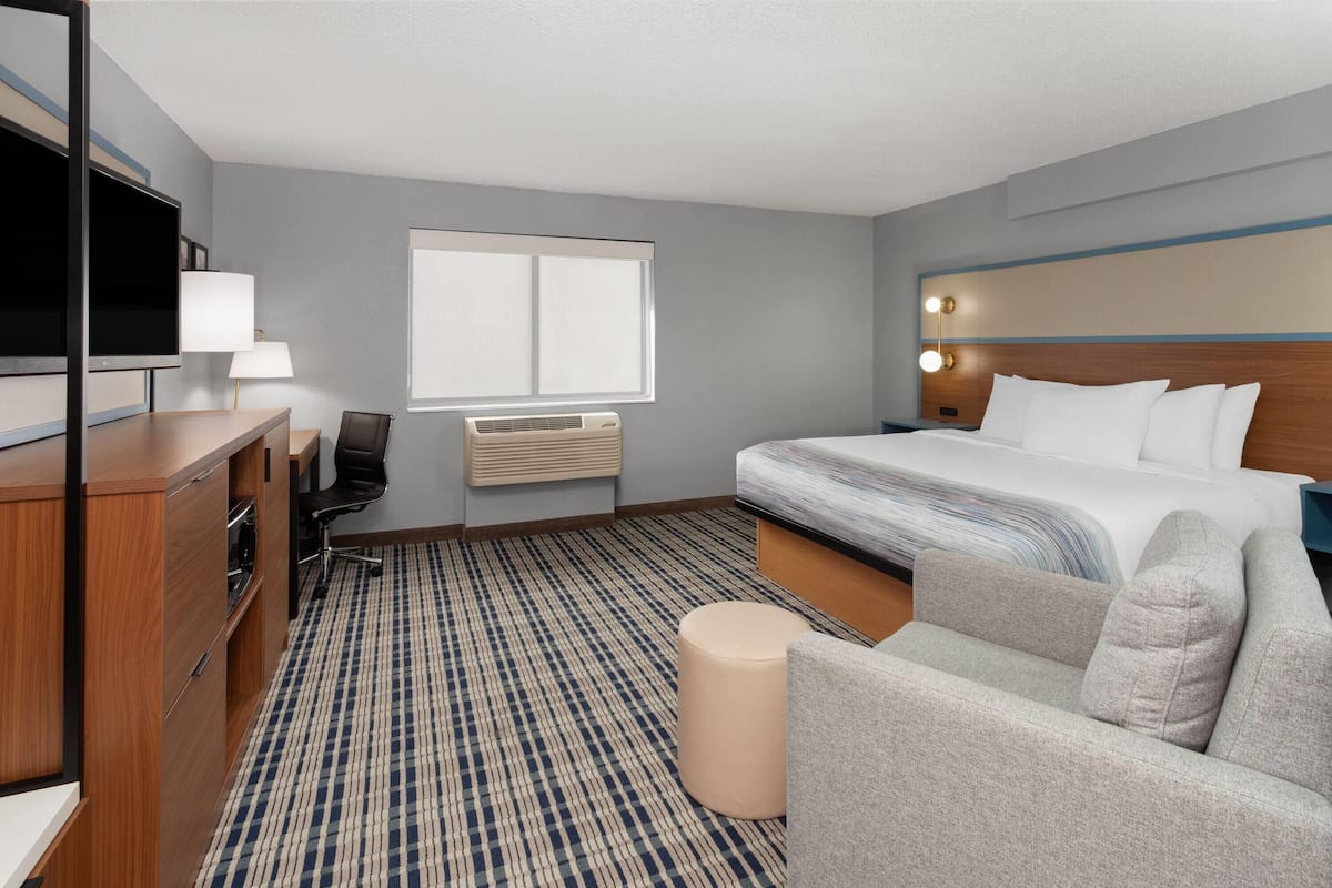 Una habitación de hotel con una cama, un escritorio con silla, televisión, lámpara y ventana.