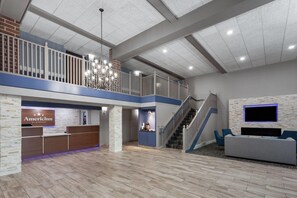 Una hall d'albergo con una reception, una scala, un'area relax e una TV a parete.